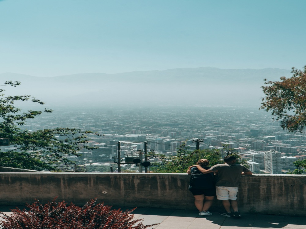 Pareja de viajeros abrazada en un mirador, contemplando una ciudad rodeada de montañas